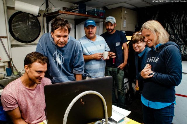 Nathan Robinson, Sonke Johnsen, Tracey Sutton, Nick Allen, Edie Widder, and Megan McCall gather around to watch the squid video. Image courtesy of Danté Fenolio via NOAA